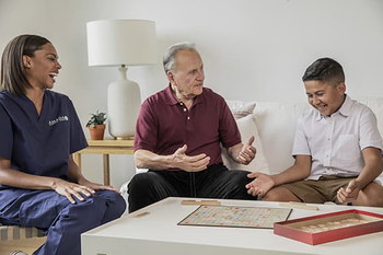 Caregiver and senior client enjoy quality time playing board game with client's grandson.